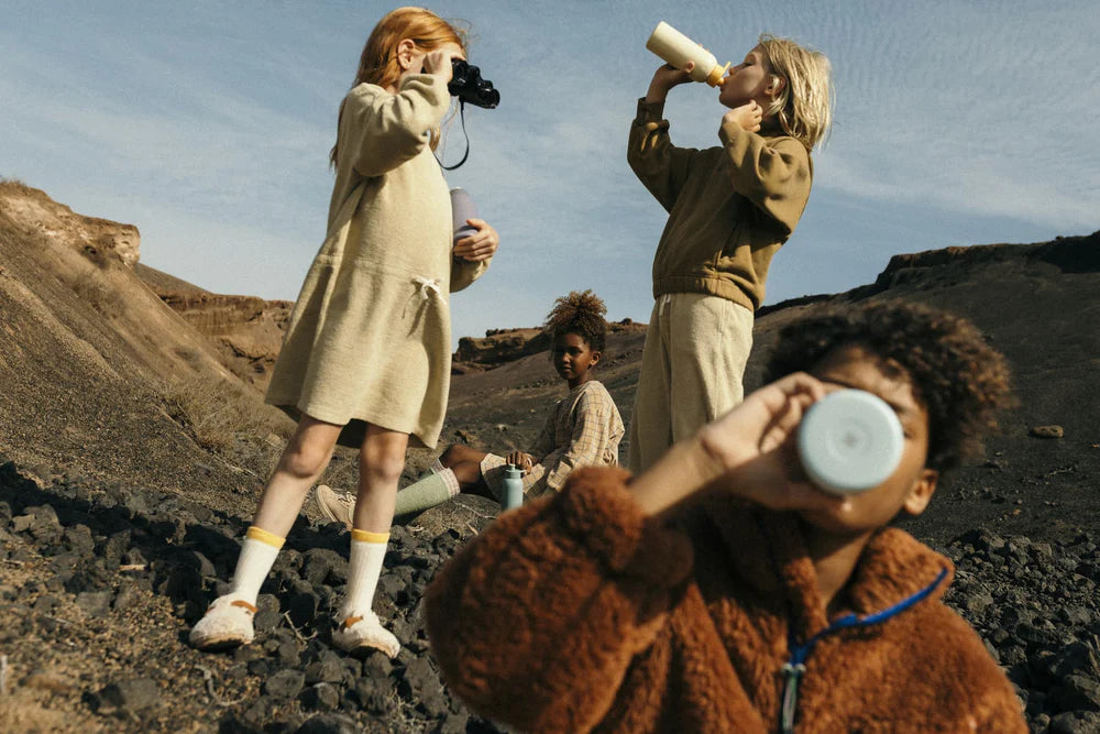 A group of children outdoors, each holding and drinking from waterdrop kids bottles, with a rugged, natural landscape in the background.