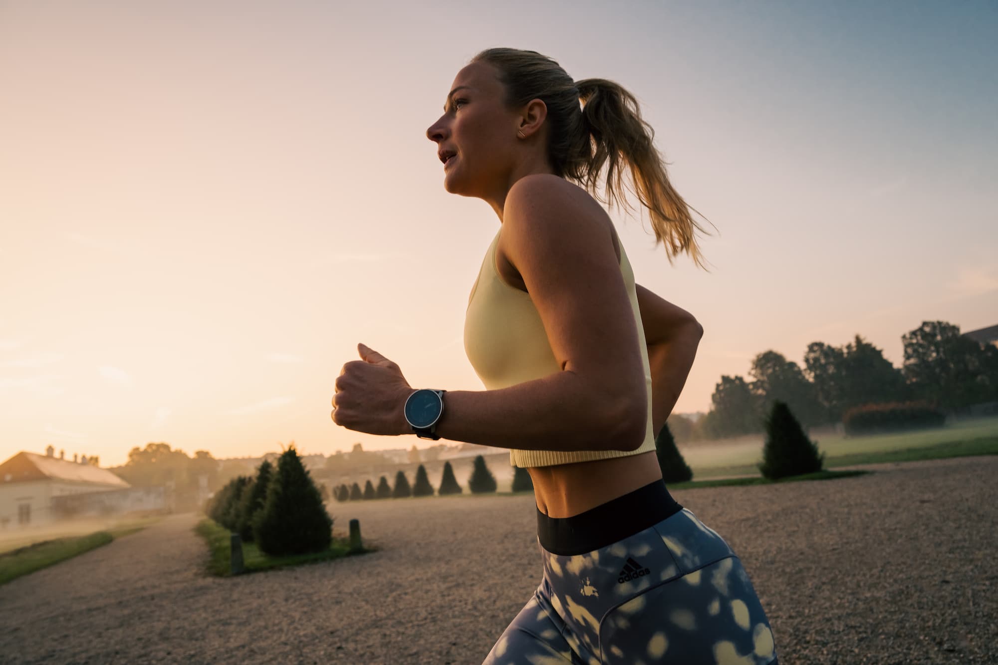 Fit woman running at sunrise, wearing a smart watch and athletic wear, embracing an active lifestyle and morning fitness routine.