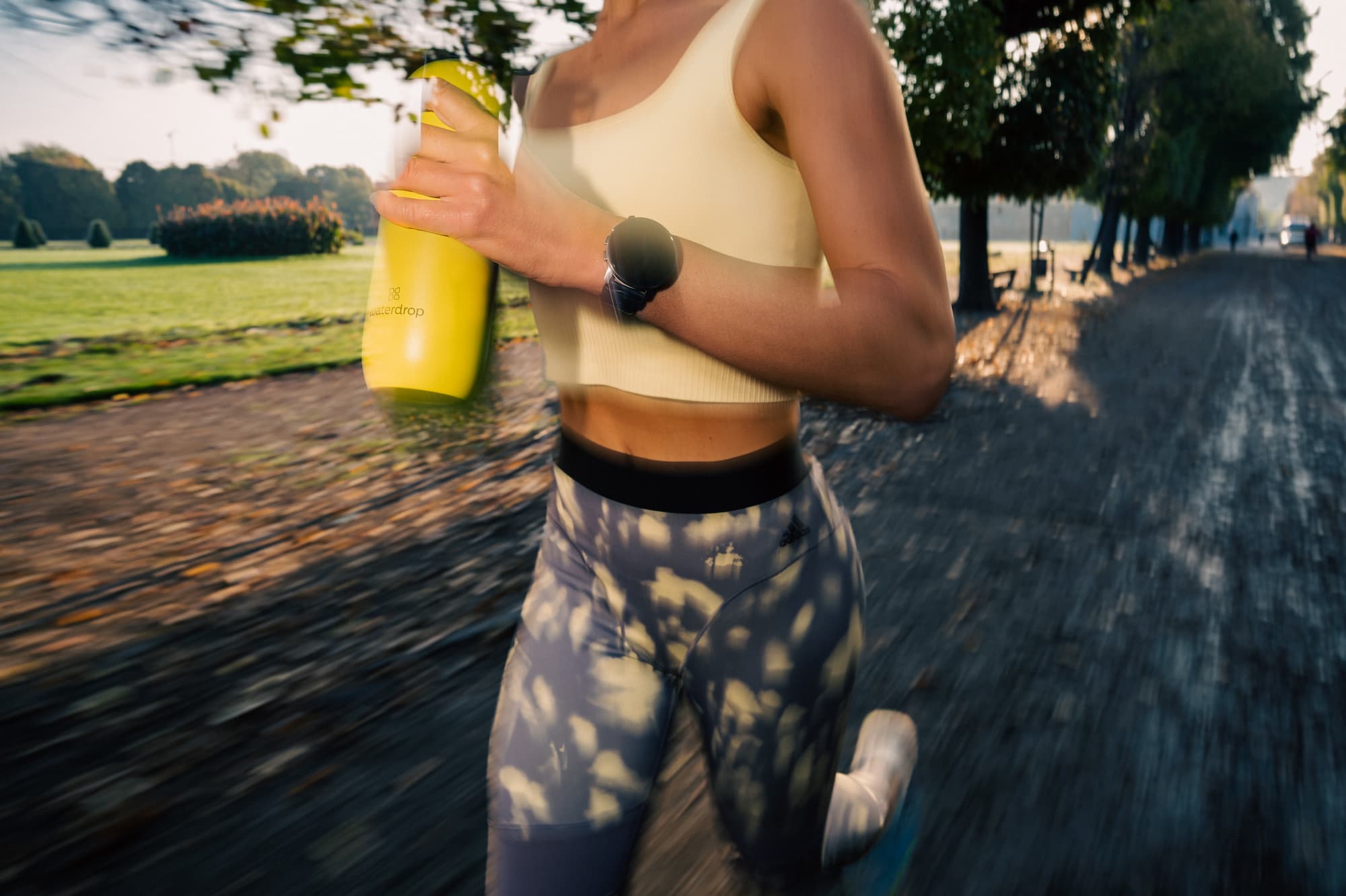 A woman is running outdoors holding a yellow waterdrop bottle in her hand