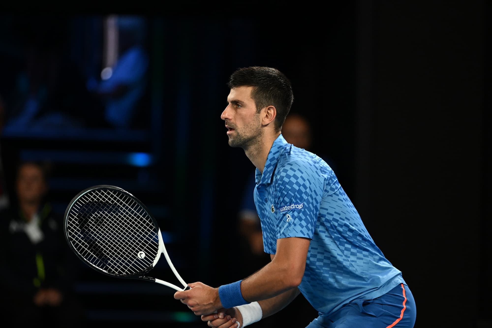 Novak Djokovic on the tennis court holding a tennis racket in his hands, ready to play