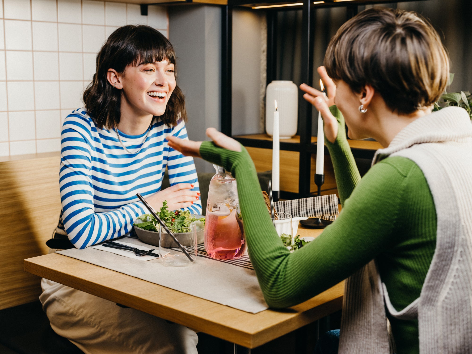 Two women enjoying a meal and conversation in a cozy restaurant with a waterdrop carafe filled with a pink beverage on the table.