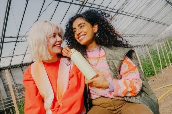 Blond woman sitting next to a field holding a waterdrop®  steel bottle in her hands