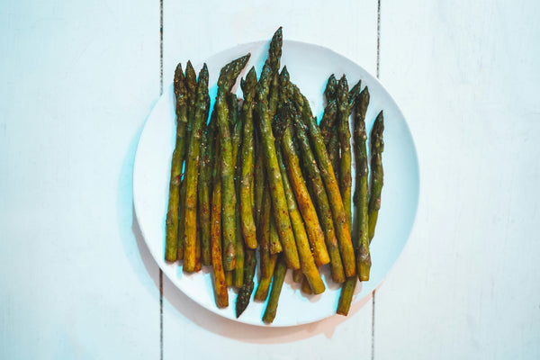 Plate of roasted asparagus spears seasoned with spices on a white wooden background.