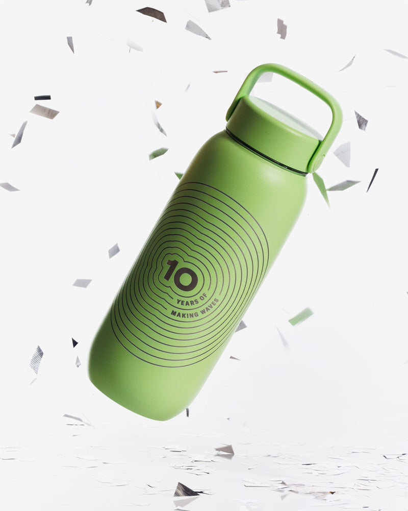 Green reusable water bottle with a top handle, tilted against a white background with confetti.
