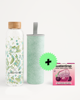 Glass water bottle with a floral pattern and wooden cap, a mint-green insulated bottle, and a small pink flavor-drops package.