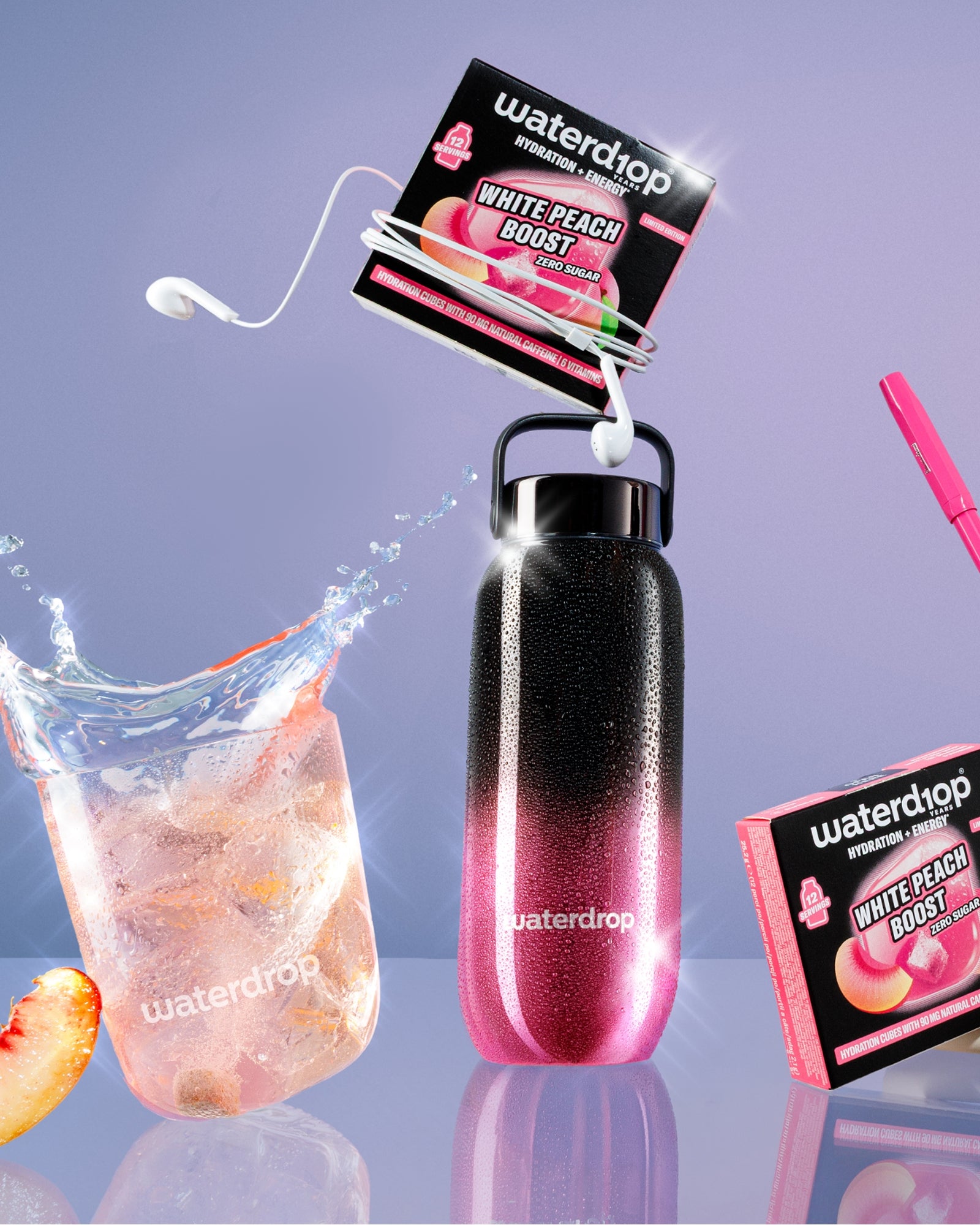 Gradient pink-to-black reusable bottle with a loop handle, attached flavor packets, a glass of ice with a peach slice, and a pink straw accessory.