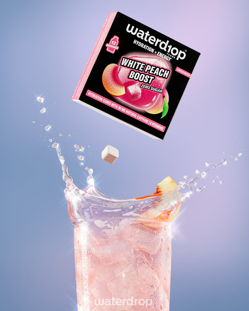 Box descending toward a tall glass of pink peach-flavored beverage with peach pieces, creating a splash.