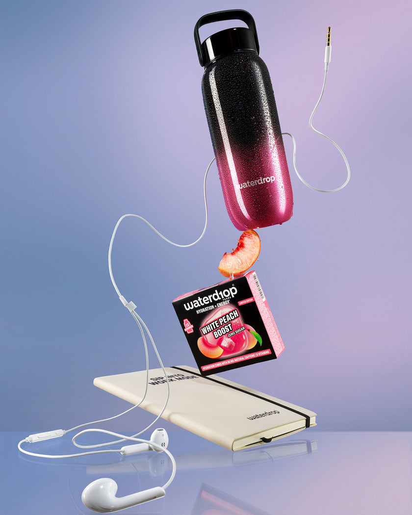Floating display of a black-to-pink gradient water bottle above a white power bank, connected by white cords with a peach slice nearby.