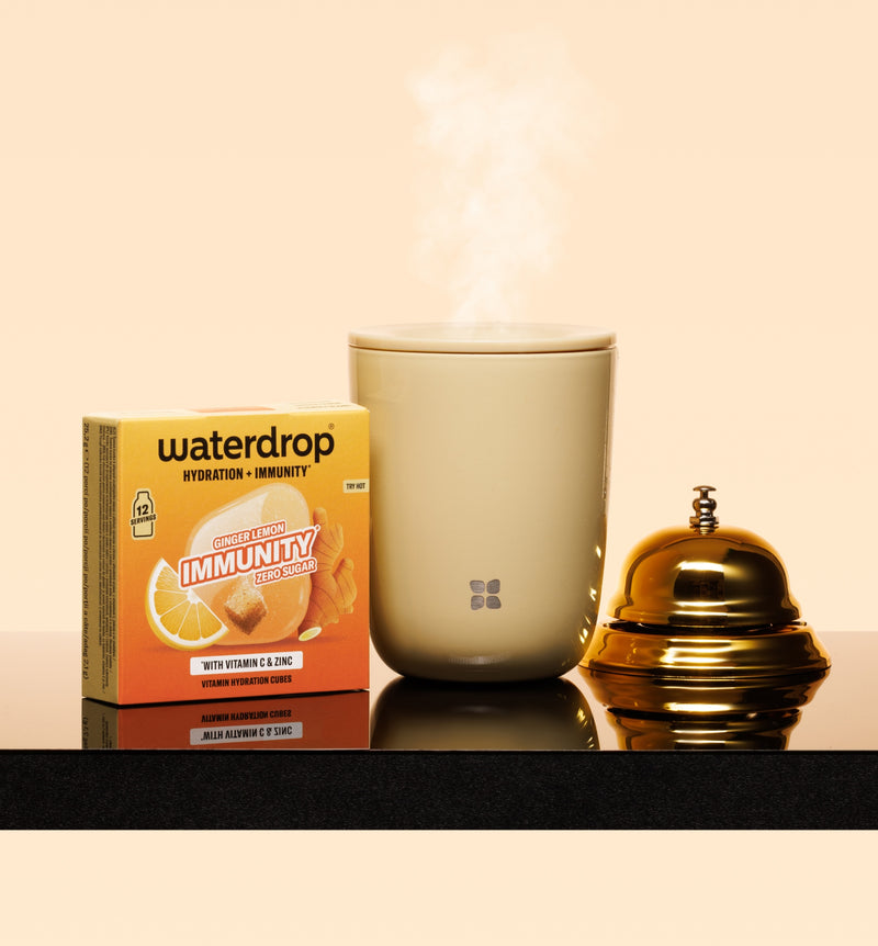 Steaming beige mug on a dark countertop beside a box and a gold-toned, domed container.
