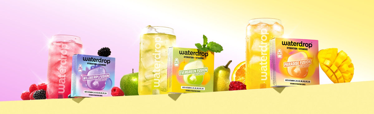 Assorted Waterdrop flavor enhancers in pink, purple, green, and yellow bottles on a yellow shelf with fruit.