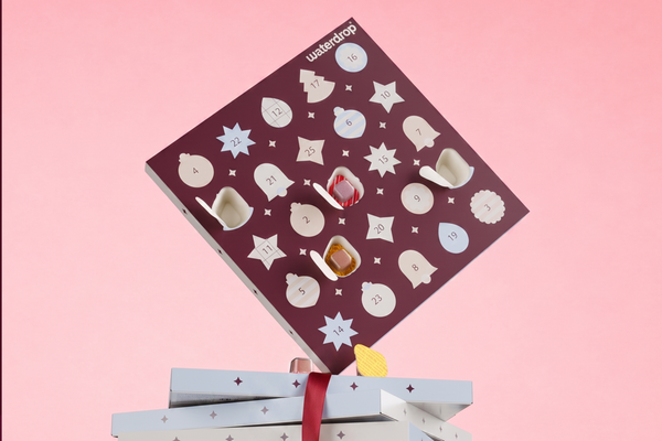 Advent calendar with circular windows and small items atop wrapped gifts against a pink background.