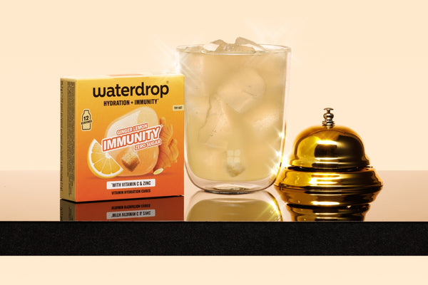 Hydration product box, a glass of iced water, and a gold service bell on a dark countertop.