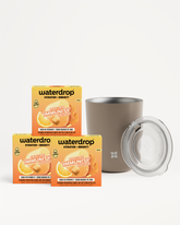 Three orange boxes of a hydration product displayed next to a beige tumbler with a clear lid.